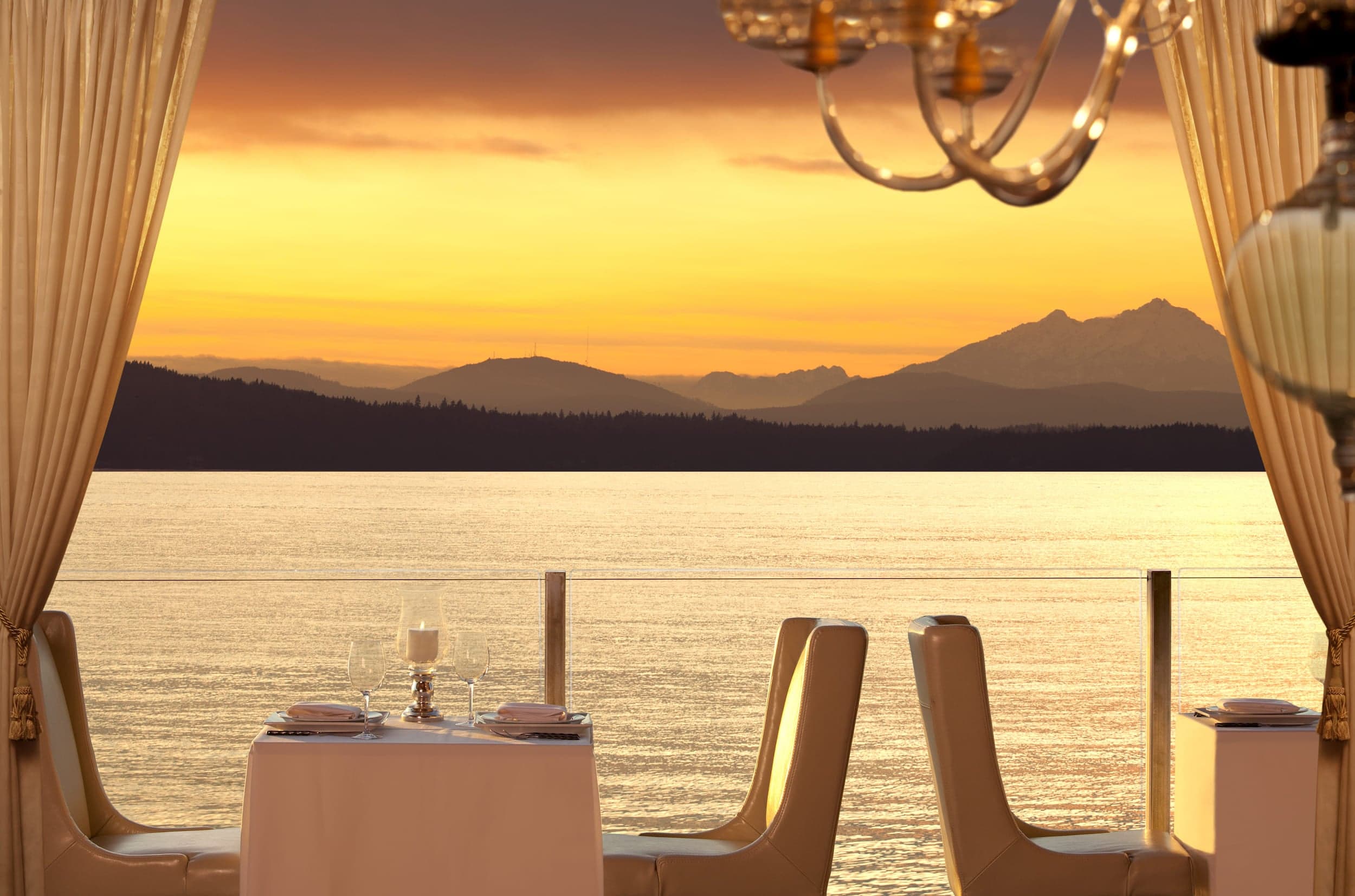 A sunset lit dining room on the water with beautiful mountains in the background
