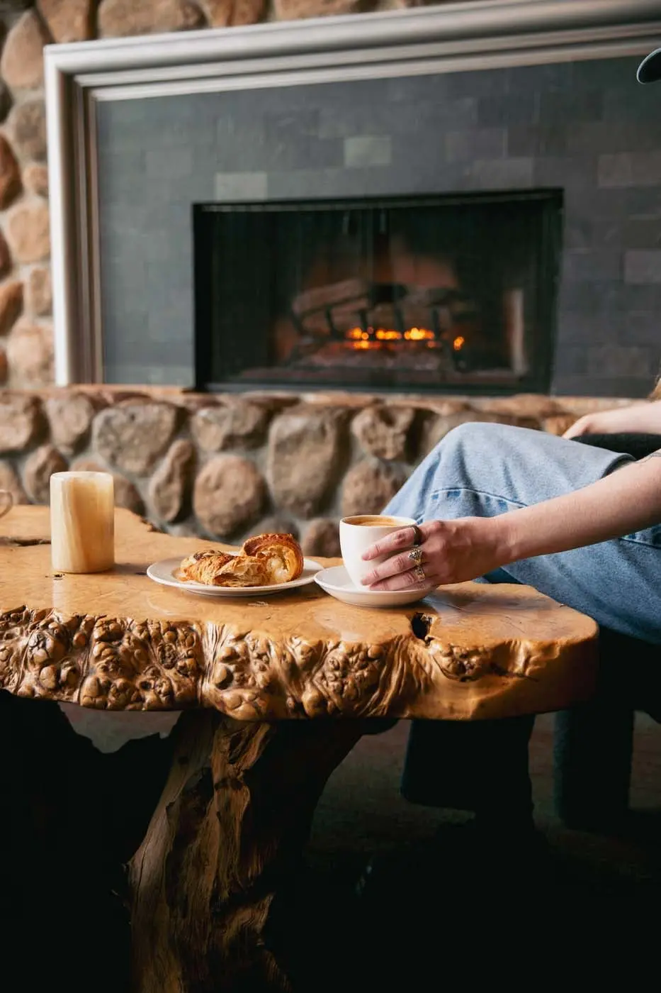 A fresh pastry and hot beverage on a live edge wood table in front of the fireplace at Edgewater